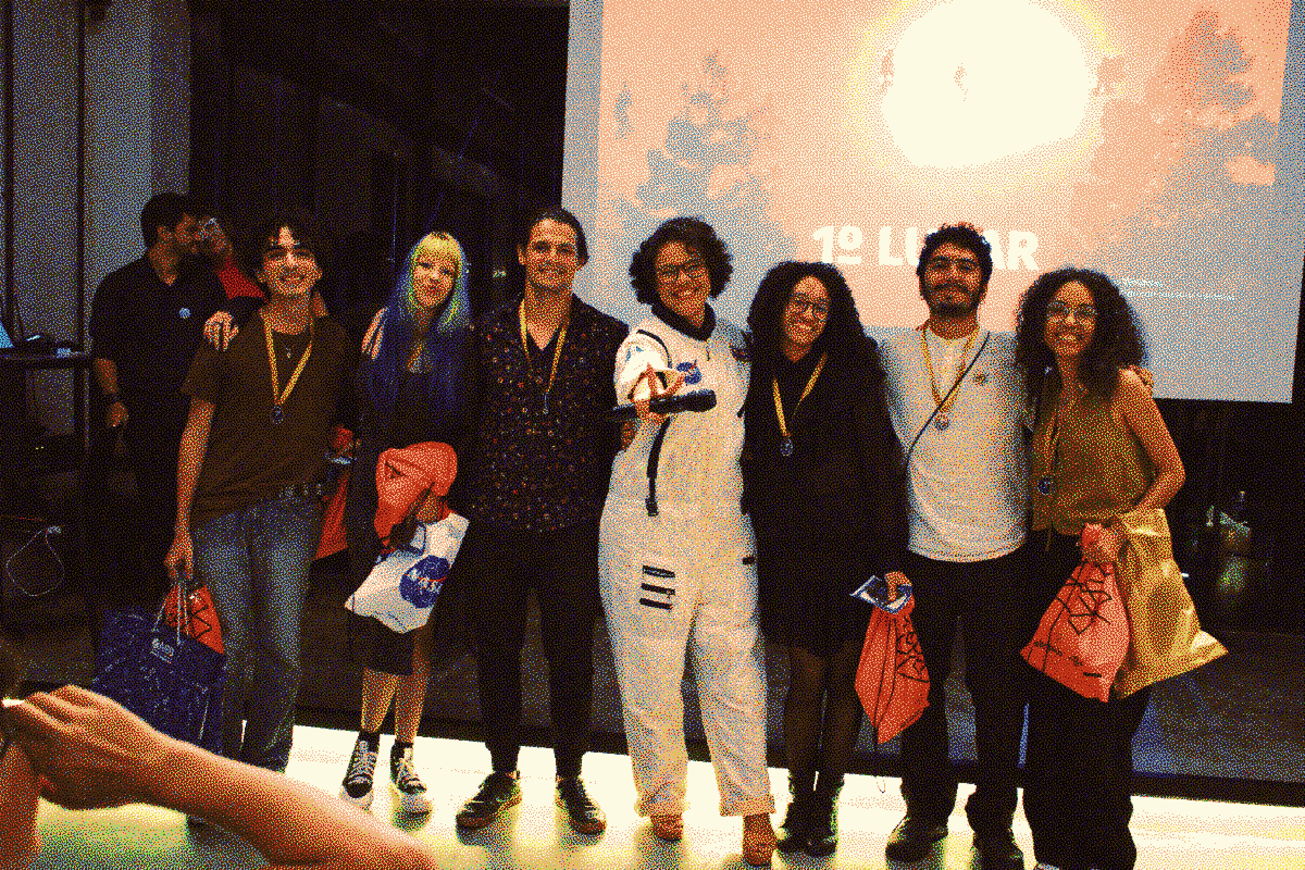 Fotografia da equipe reunida com Dani Bezerra, líder local da competição, com medalhas em seus pescoços e prêmios em suas mãos